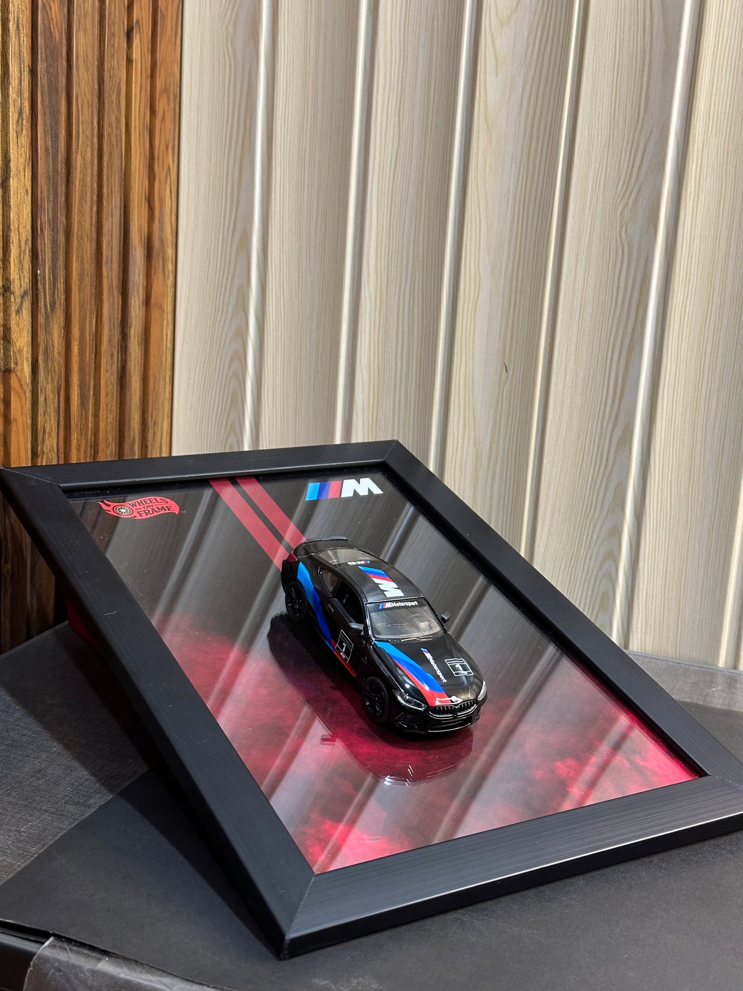 Framed BMW M 8 on a reflective surface with a wooden and white paneled background