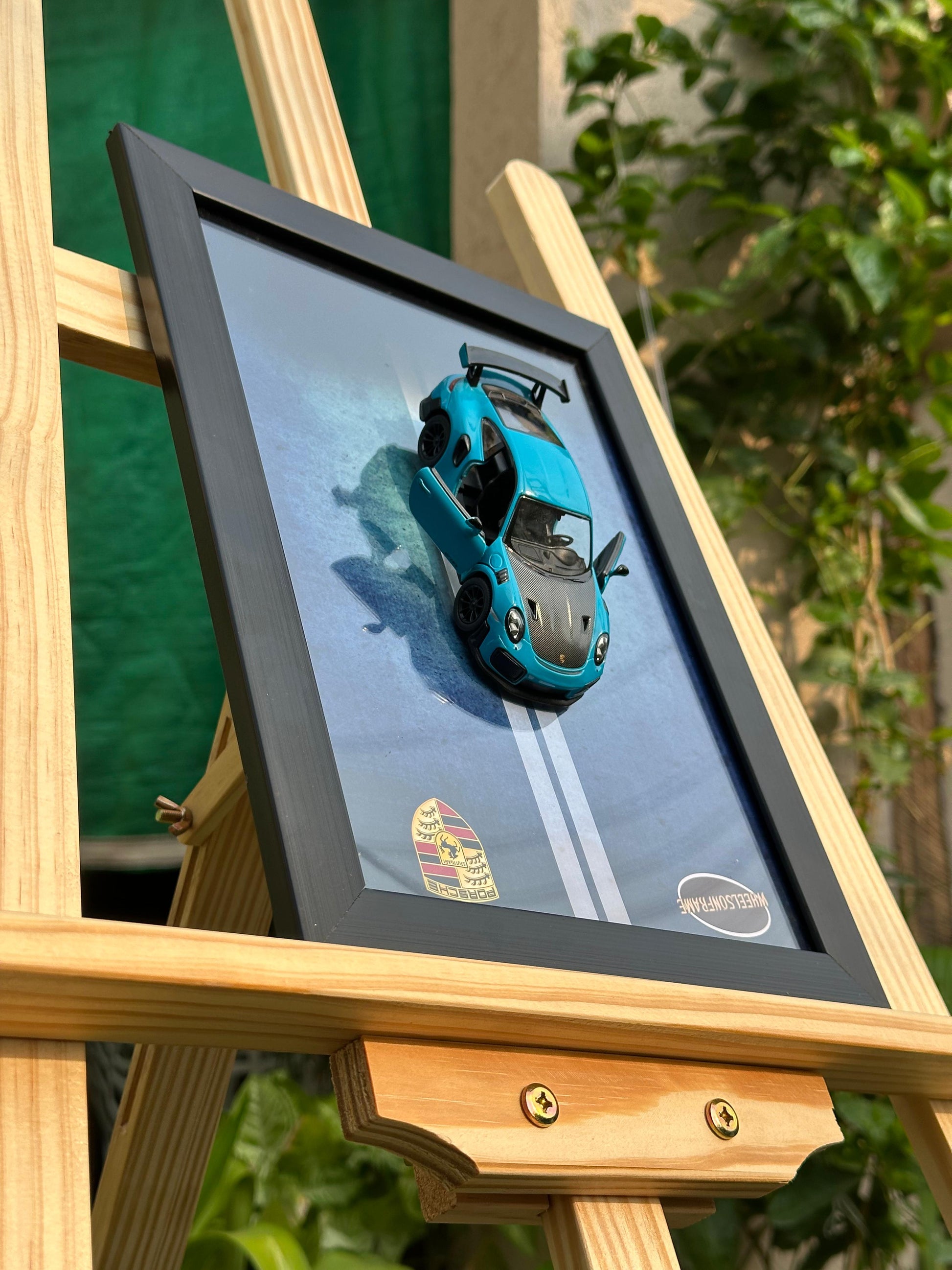 Framed artwork of a blue car on a wooden easel with a blurred green background